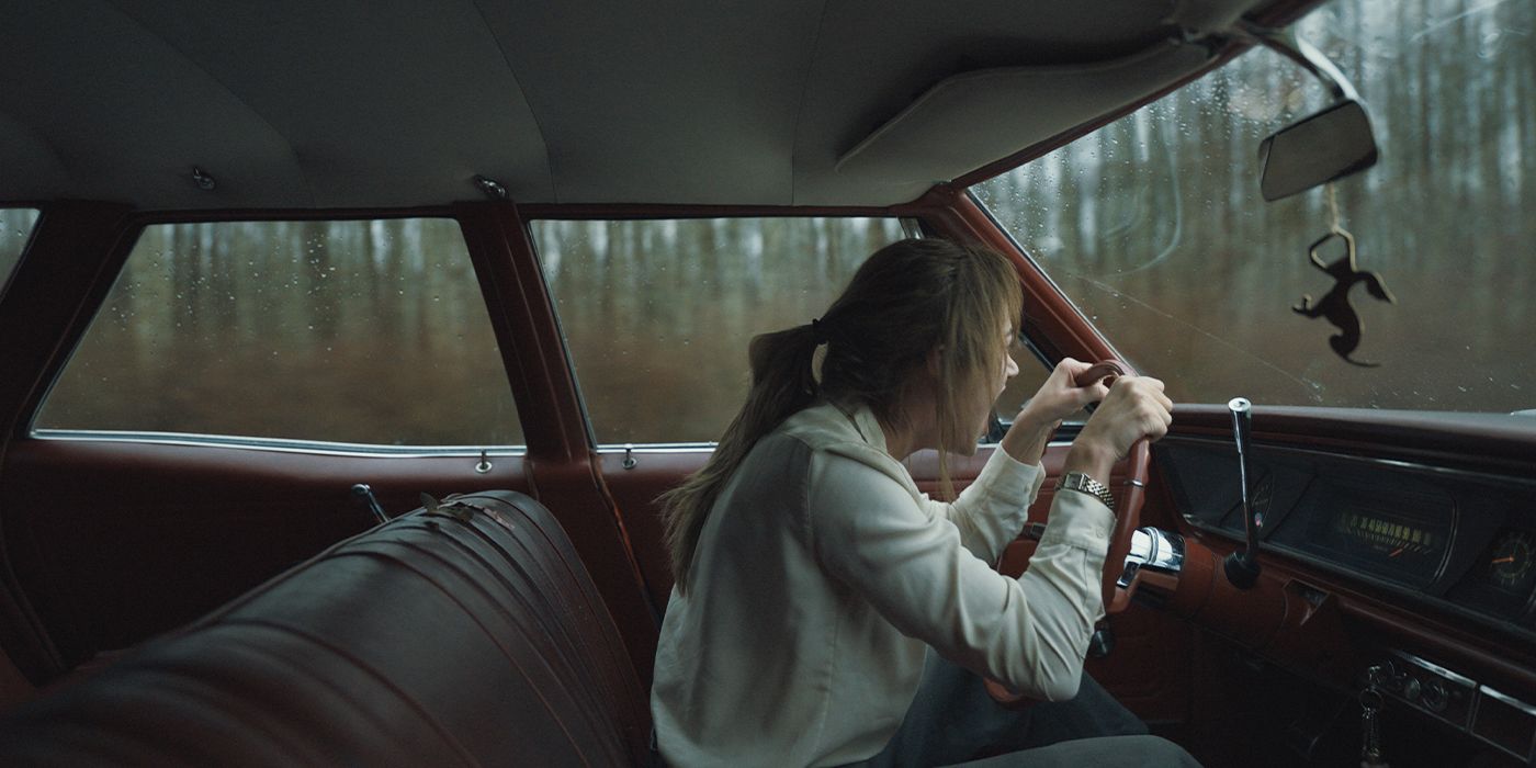 Maika Monroe está al volante de su coche, inclinándose hacia adelante y gritando.