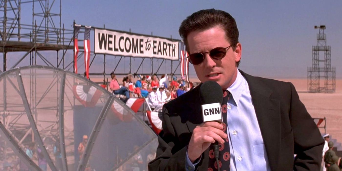 Newsman Jason Stone (Michael J. Fox) speaks to the camera as a small crowd sit in a stand behind him in the desert, waiting for the aliens to arrive in 'Mars Attacks!' (1996).