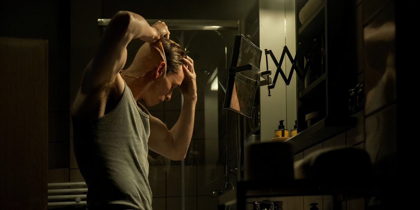 eddie redmayne wears a tank top and pulls off his bald cap as his disguise in 'The Day of the Jackal'