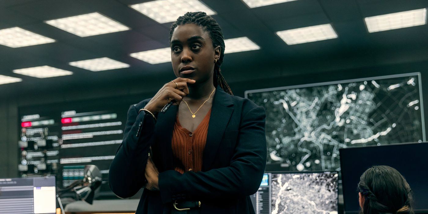 Lashana Lynch wears an orange shirt with a black suit coat over it and looks pensive