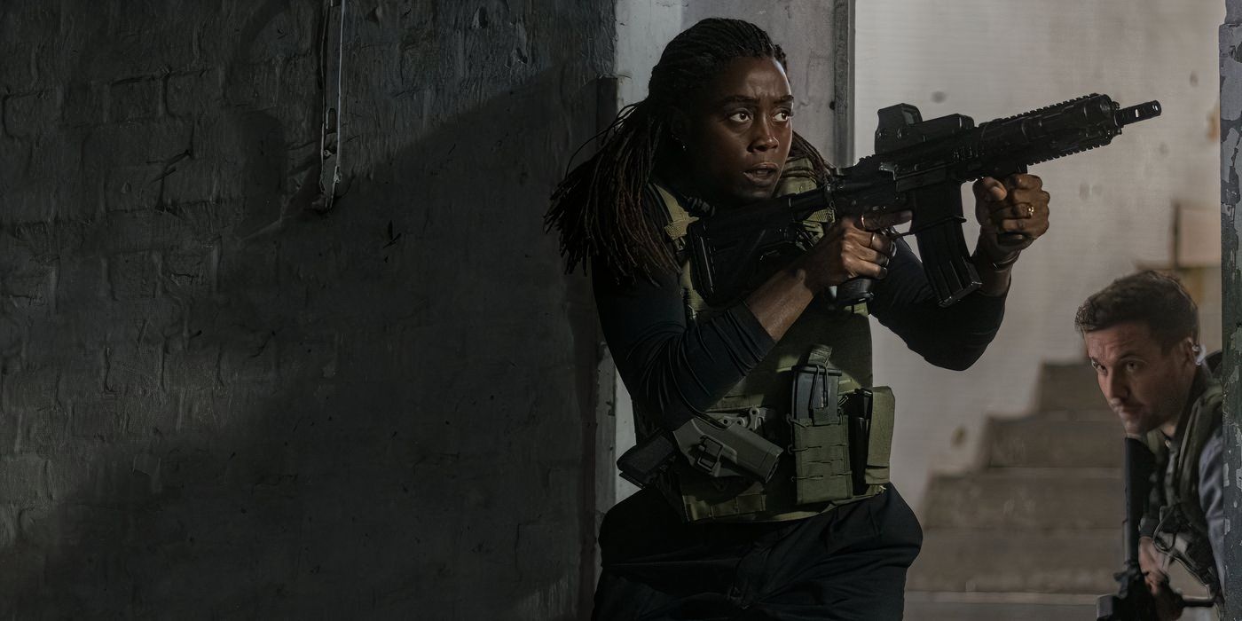 Lashana Lynch is dressed in protective gear and a vest and holds an assault rifle