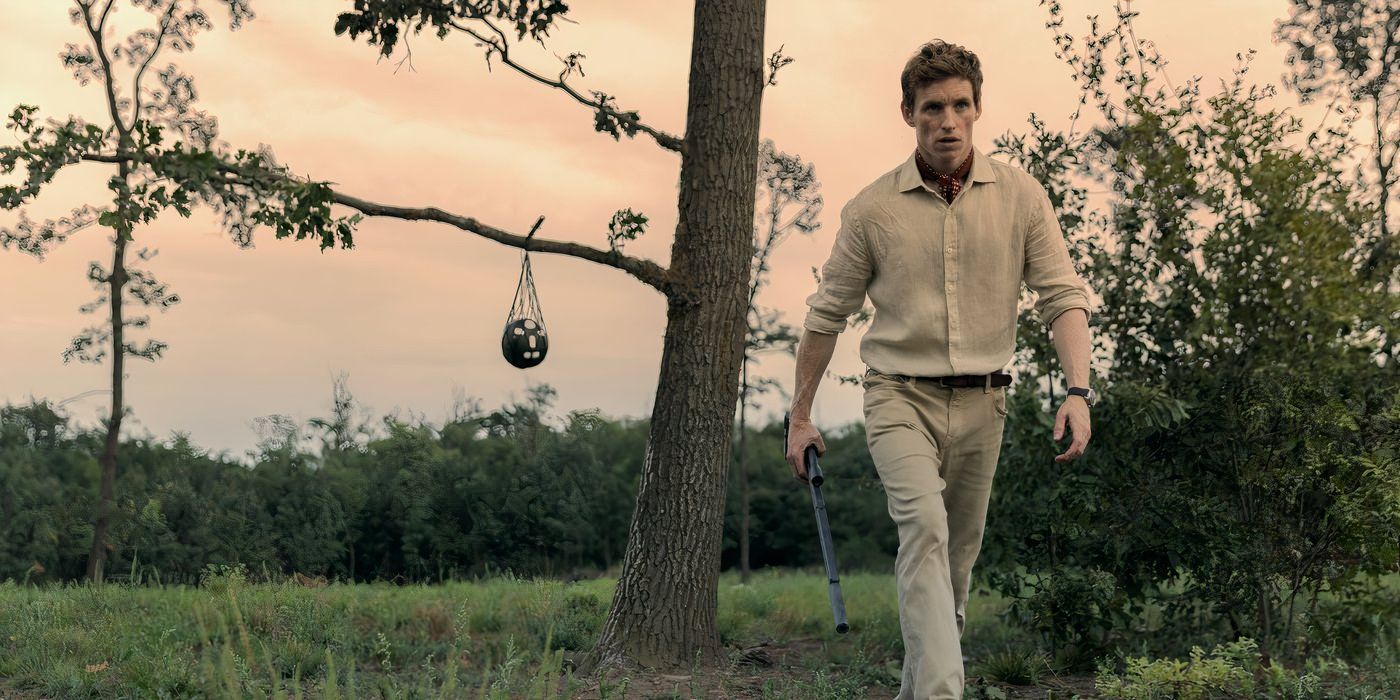 eddie redmayne wears an all white outfit and walks outside while holding onto a weapon