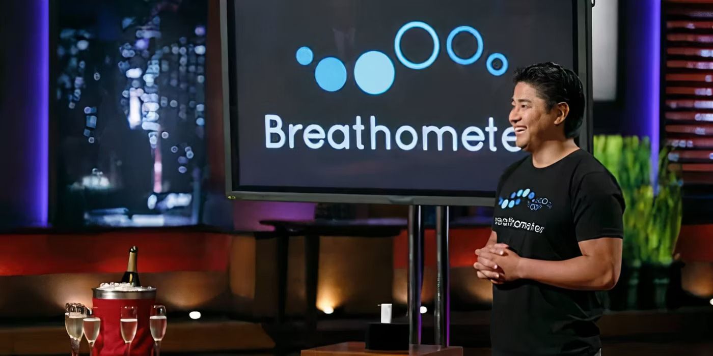 A man smiling on Shark Tank with a monitor showing Breathometer and four glasses of champagne in front