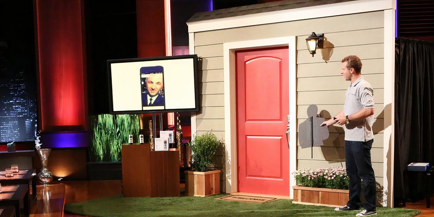 Jamie Siminoff standing on the Shark Tank stage with a model front door and screen showing Kevin's face.