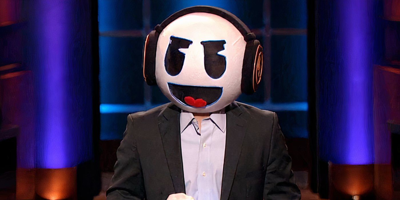 A man in a suit wearing a emoji costume head wearing headphones in Shark Tank