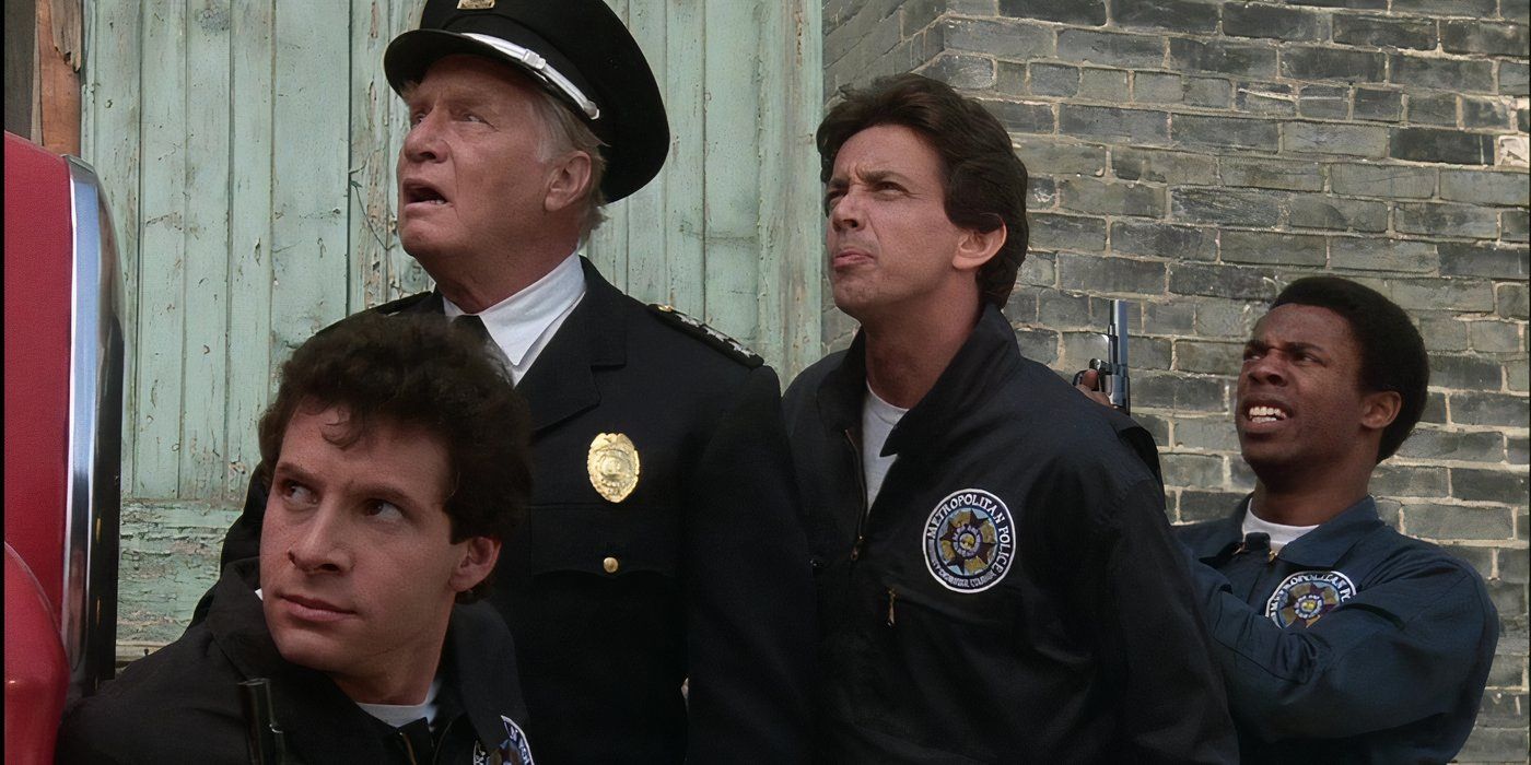 Four police officers stand against a brick building looking at something up and left off camera