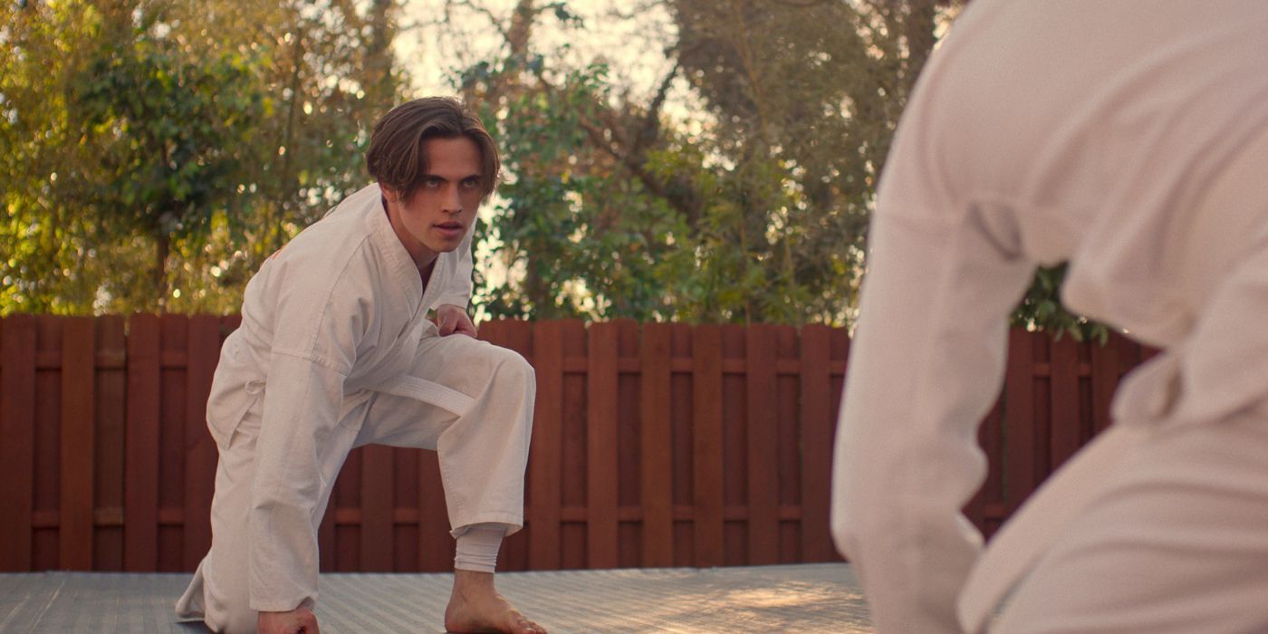 Tanner Buchanan as Robby, in a white karate gi, with his fist on the mat in Cobra Kai Season 6 Part 1.