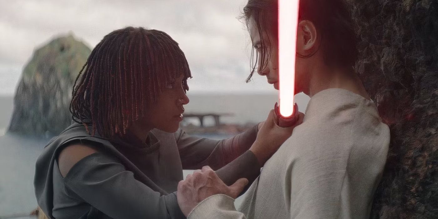 Osha (Amandla Stenberg) pinning Qimir (Manny Jacinto) to a stone wall and holding his red lightsaber at his throat, while Qimir rests his hand on her arm, in The Acolyte