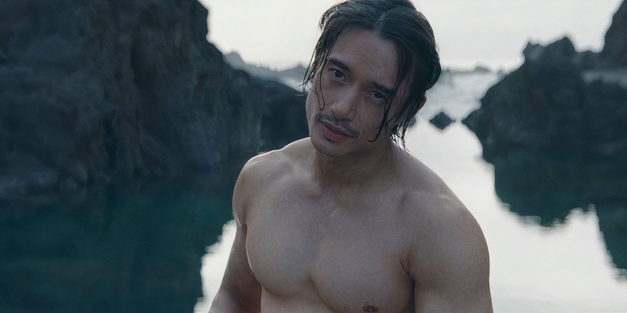 Qimir stands shirtless in front of a body of water on an unknown planet in 'The Acolyte' Episode 6