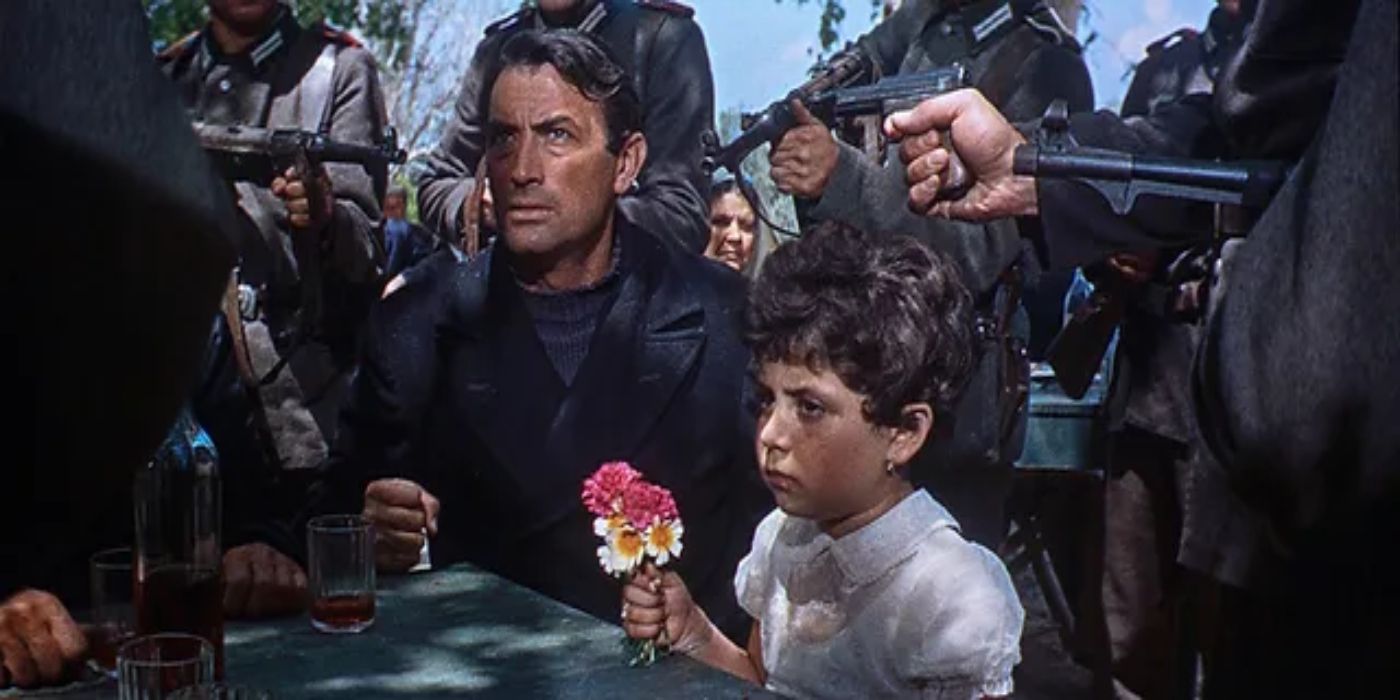 A man and a young girl sitting on a table surrounded by figures in 'The Guns of Navarone' (1961)