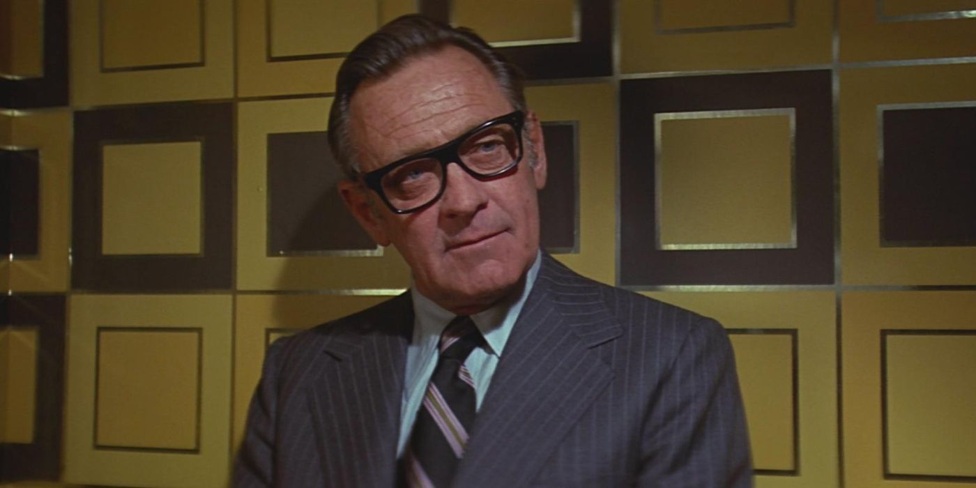 Jim Duncan (William Holden) sits against a golden wall glaring through his glasses in &lsquo;The towering Inferno&rsquo; (1970).