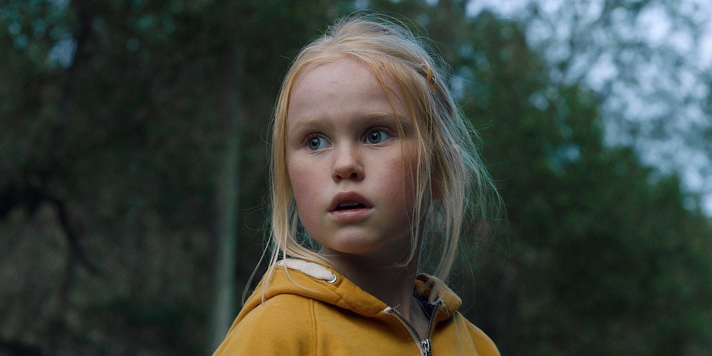 A young girl in a yellow sweater stares in fear in a forest 