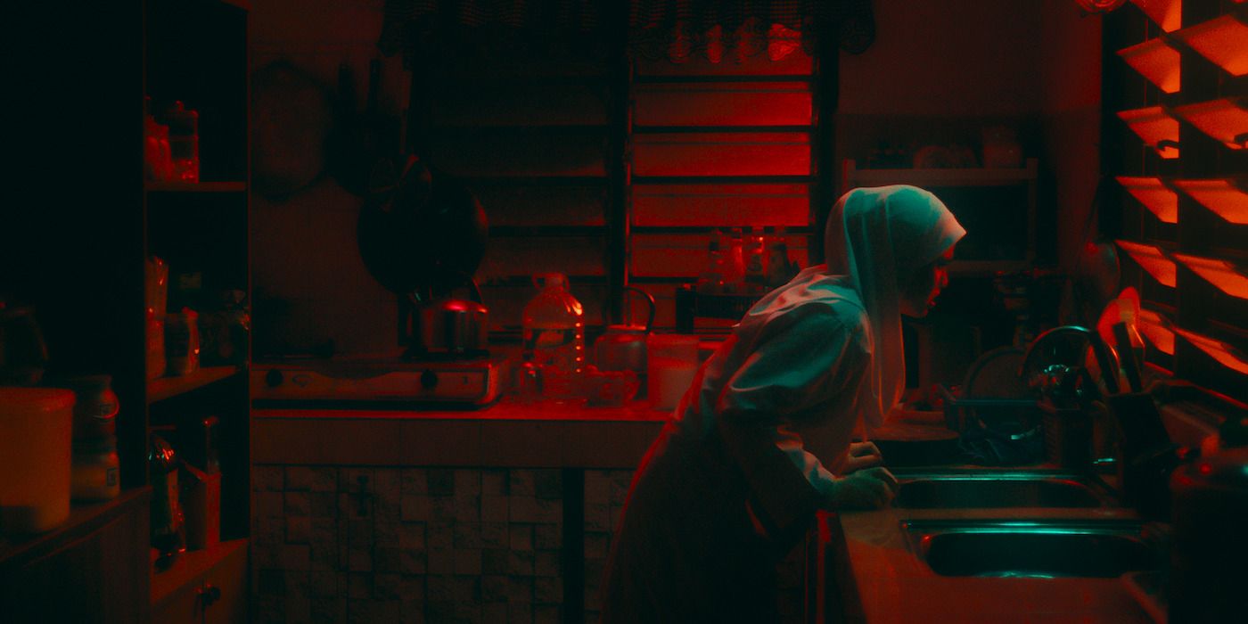 A young girl leans over a sink in a room lit by red light in Tiger Stripes. 