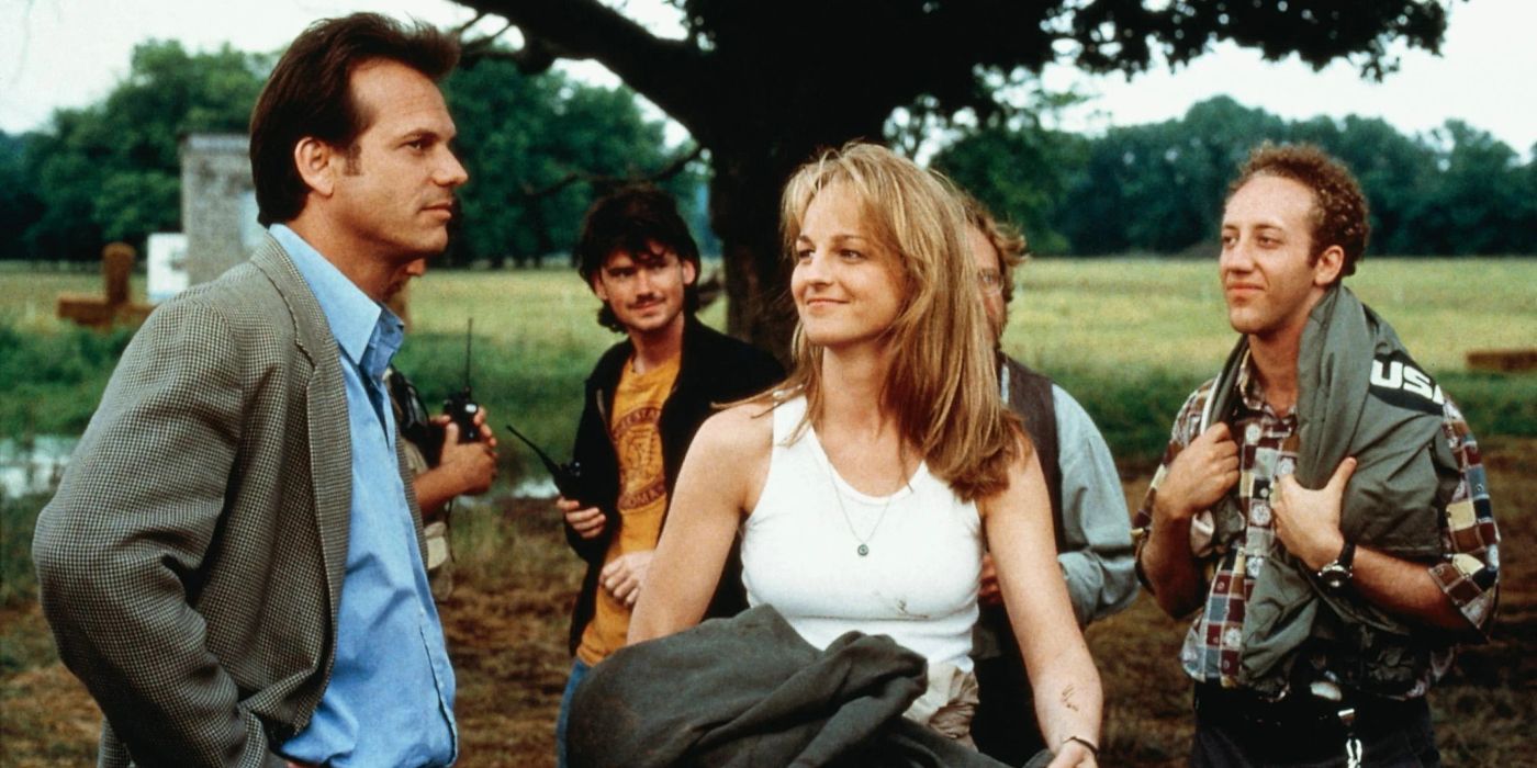 Jo Harding (Helen Hunt) smiling at a stoic BIll (Bill Paxton), who stands at her left side in front of four members of Jo's storm chasing team, in Twister