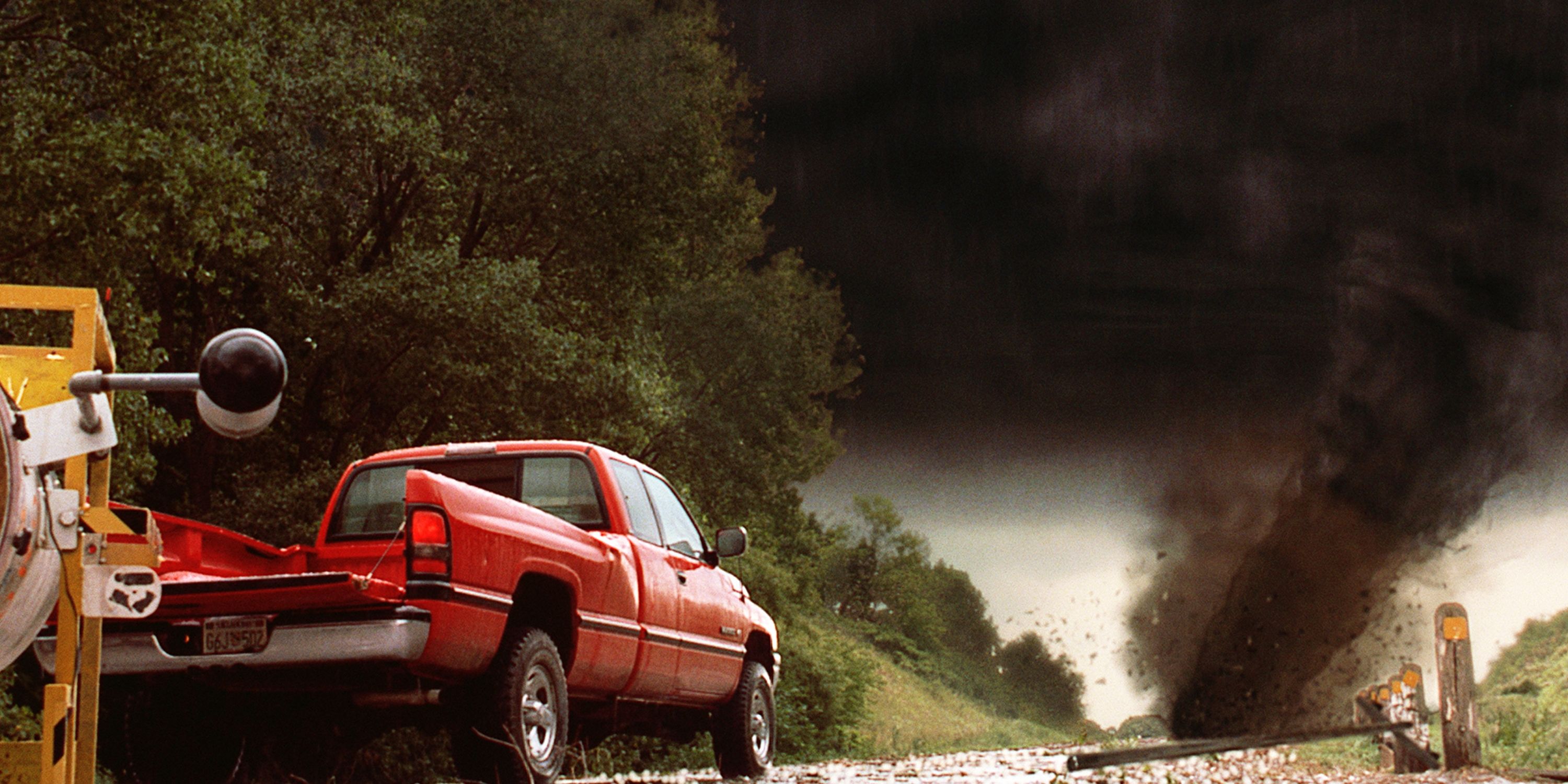 A red truck driving down a road toward a giant tornado in Twister