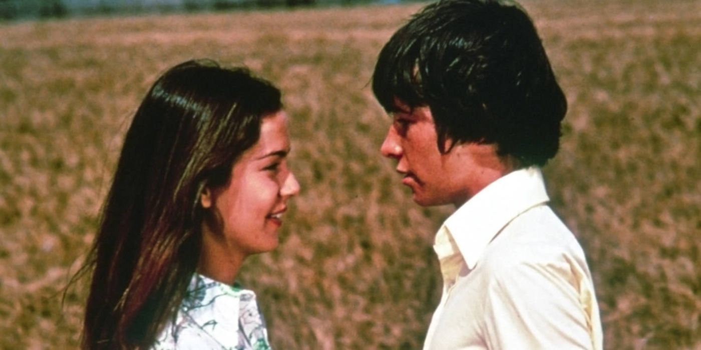 A young man and young woman smile while looking at each other in a field in Friends (1971)