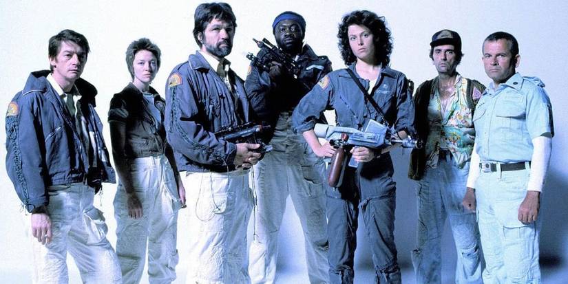 The cast stand together against a plain white backdrop and hold weapons for Alien, 1979.