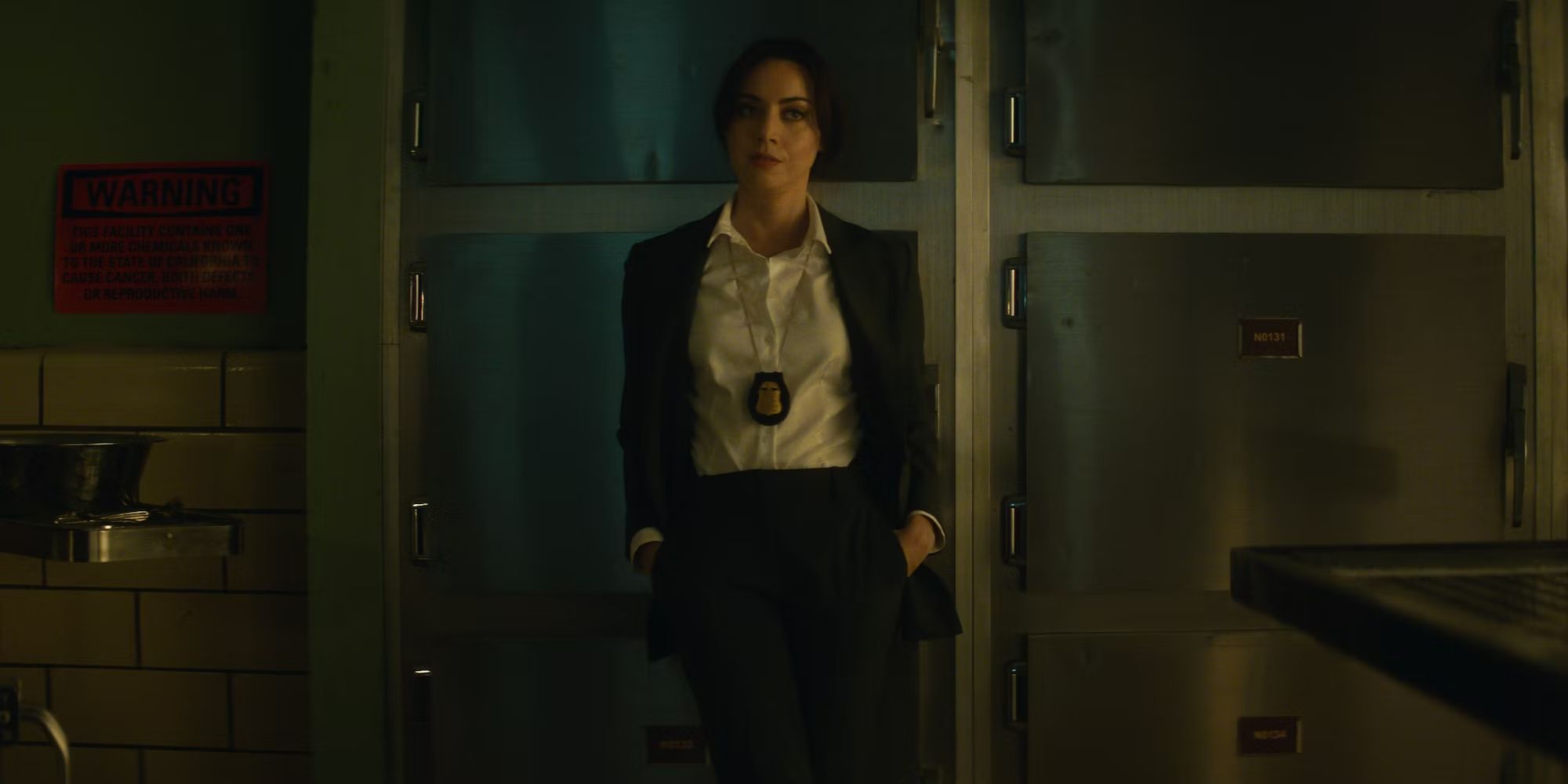 Aubrey Plaza with a police badge leaning against the wall in the morgue