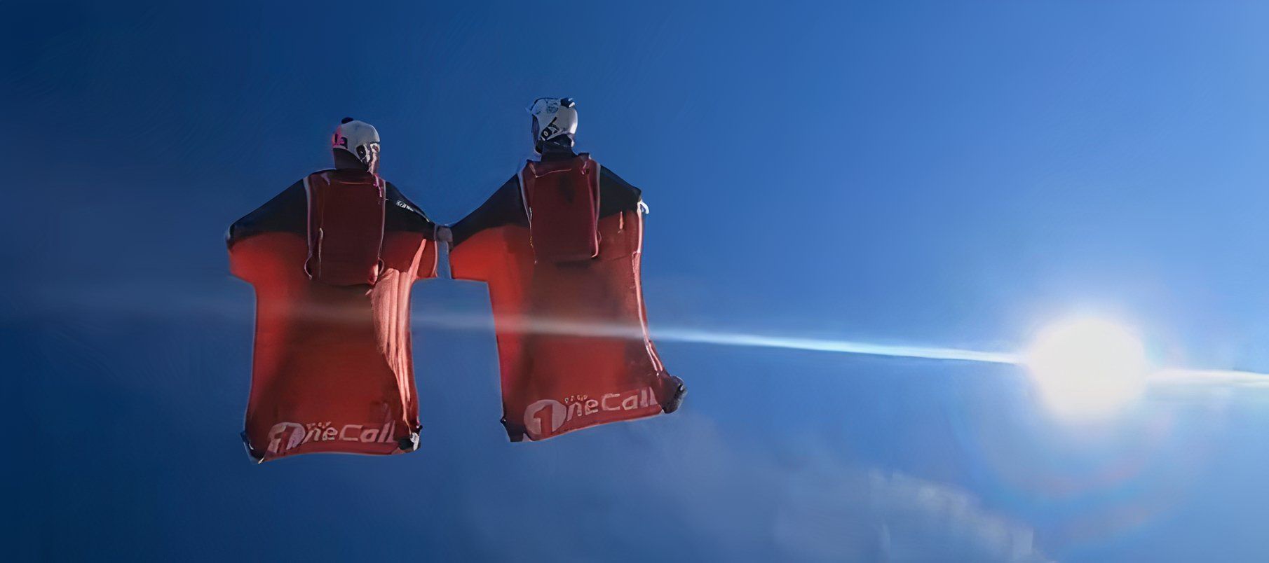 a couple of base jumpers with red suits soar through the sky