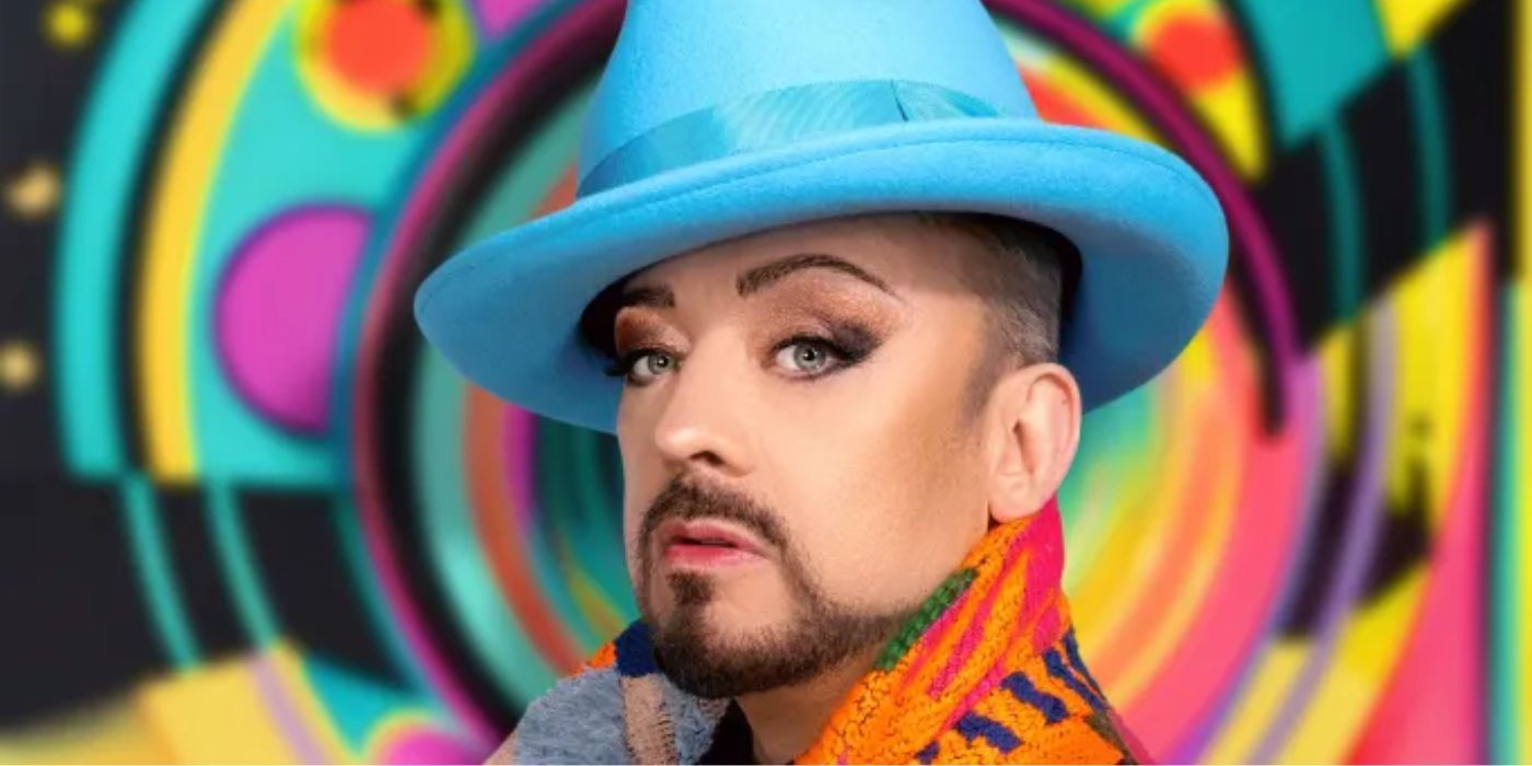 Boy George wearing a blue hat in front of a colorful background.