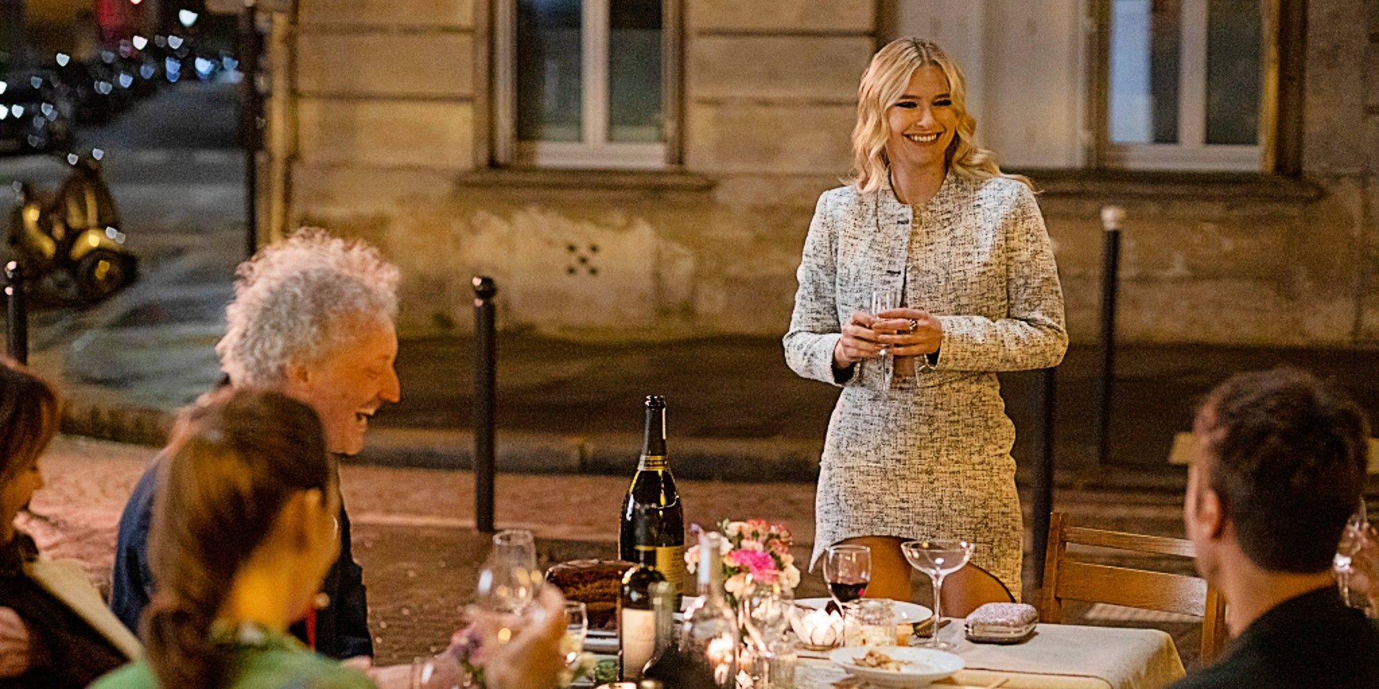 Camille stands, smiles and gives a speech at Emily's birthday dinner in Emily in Paris