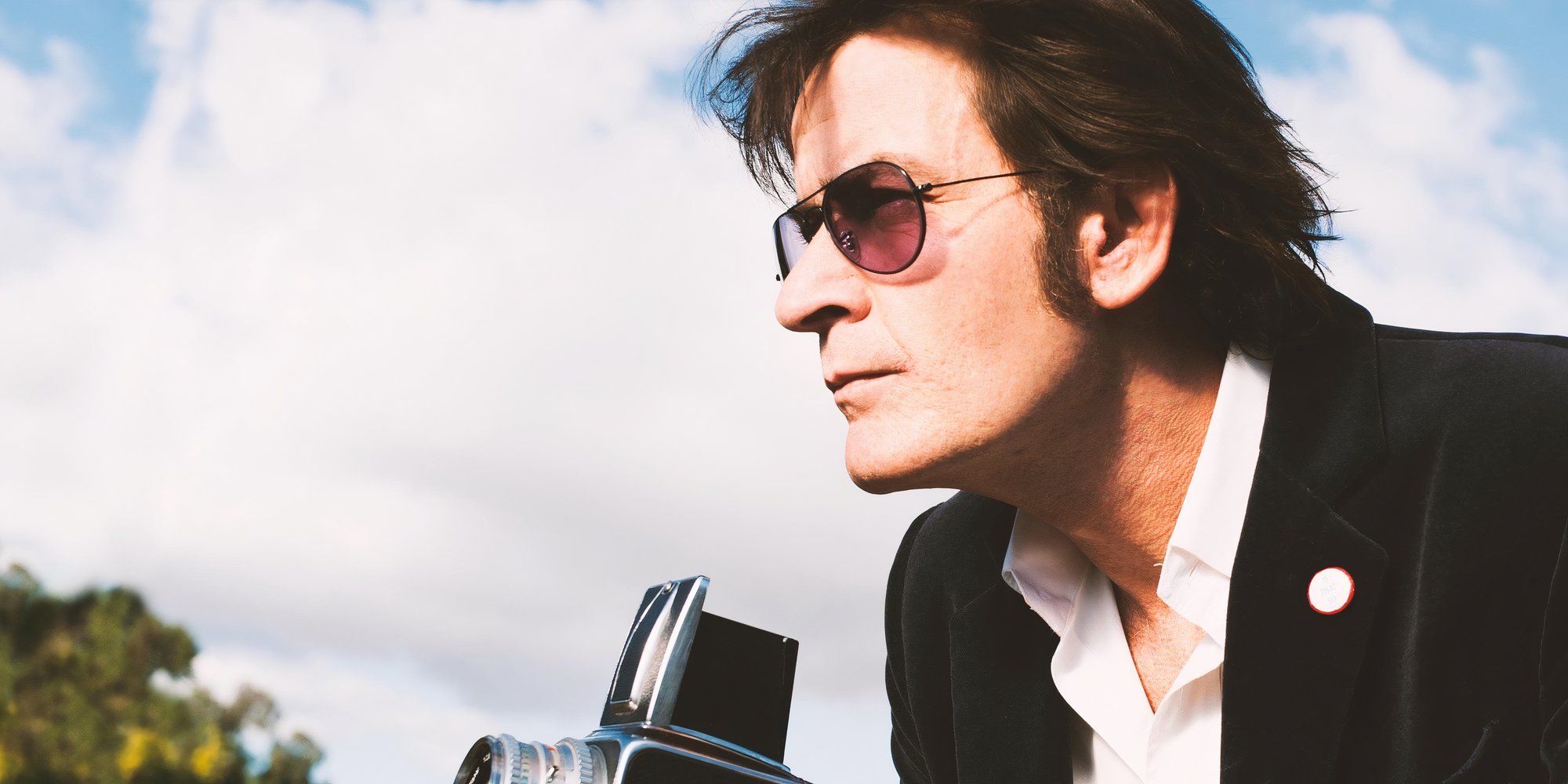 Charles Swan III holding up a camera and wearing a black suit in &lsquo;A Glimpse Inside the Mind of Charles Swan III&rsquo; (2012)