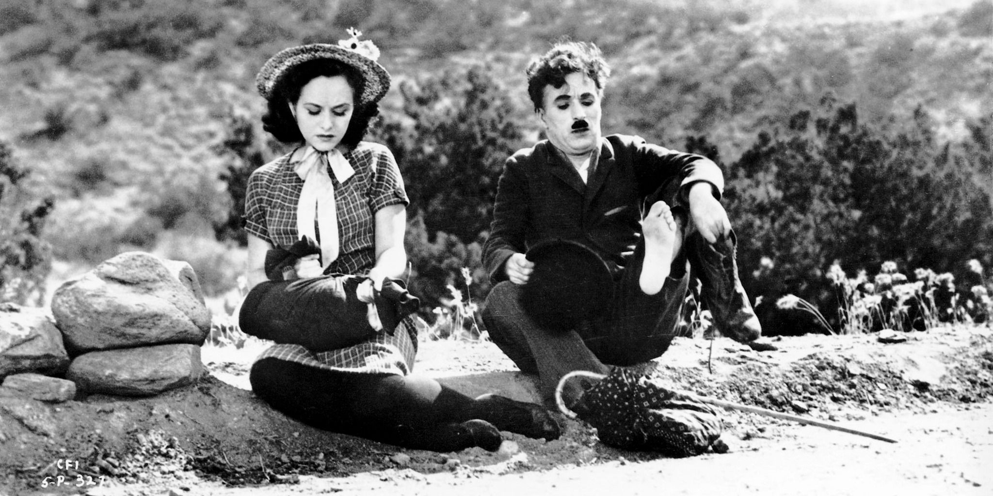 Charlie Chaplin as the Tramp and Paulette Goddard as the Gamin in 'Modern Times', sitting on the side of a dirt road