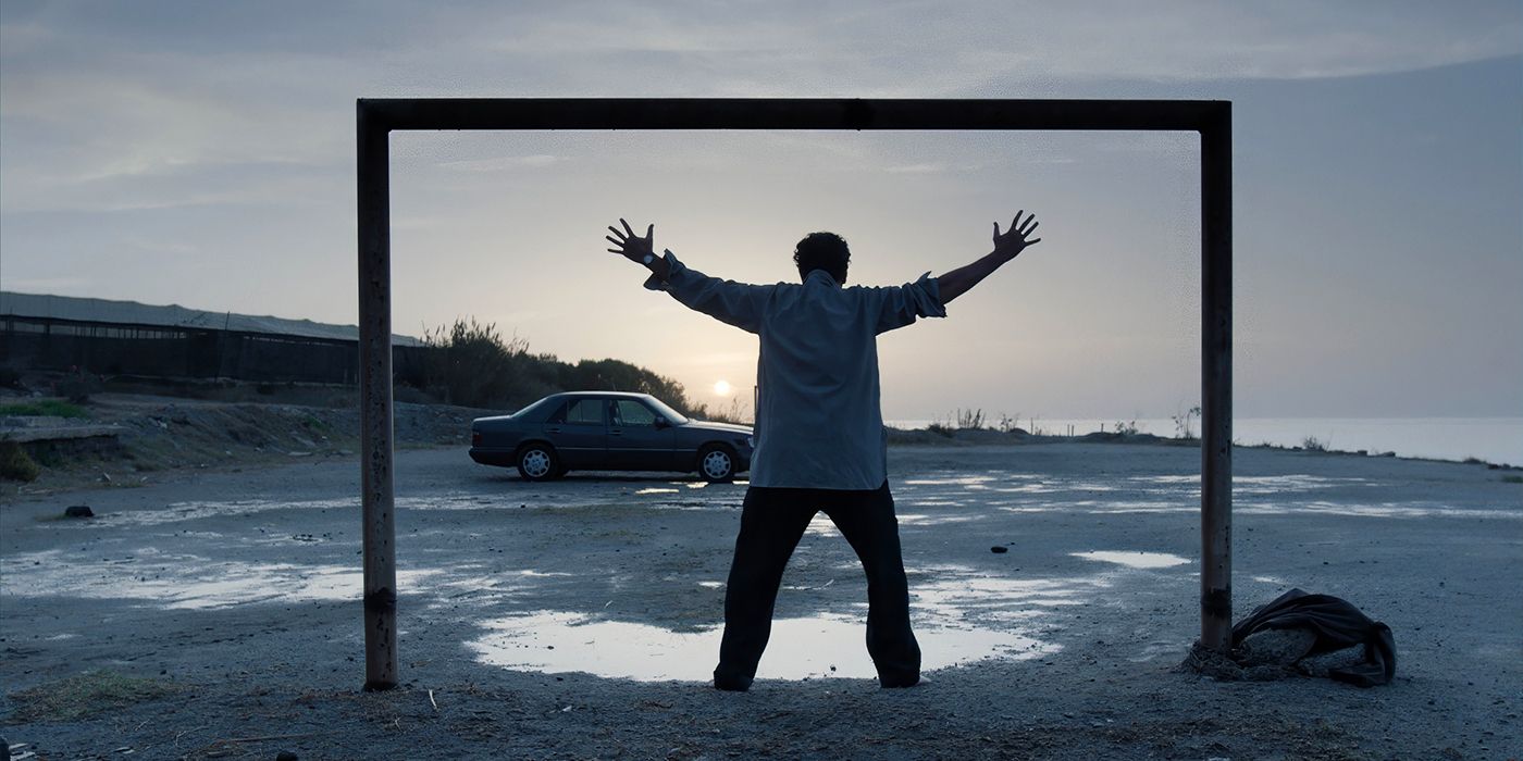 A man raises his arms as the sun rises on a soccer field in Close Your Eyes. 