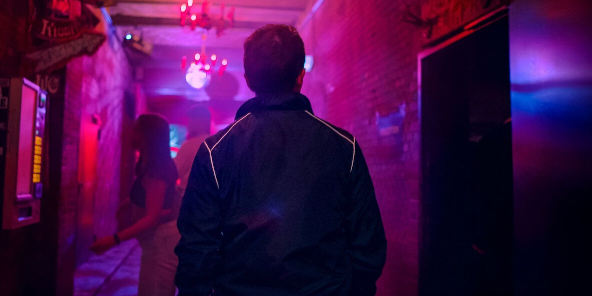 Back of a man who is walking alone down a hall lit with neon lights in Crime Scene Berlin: Nightlife Killer (2024)_Netflix