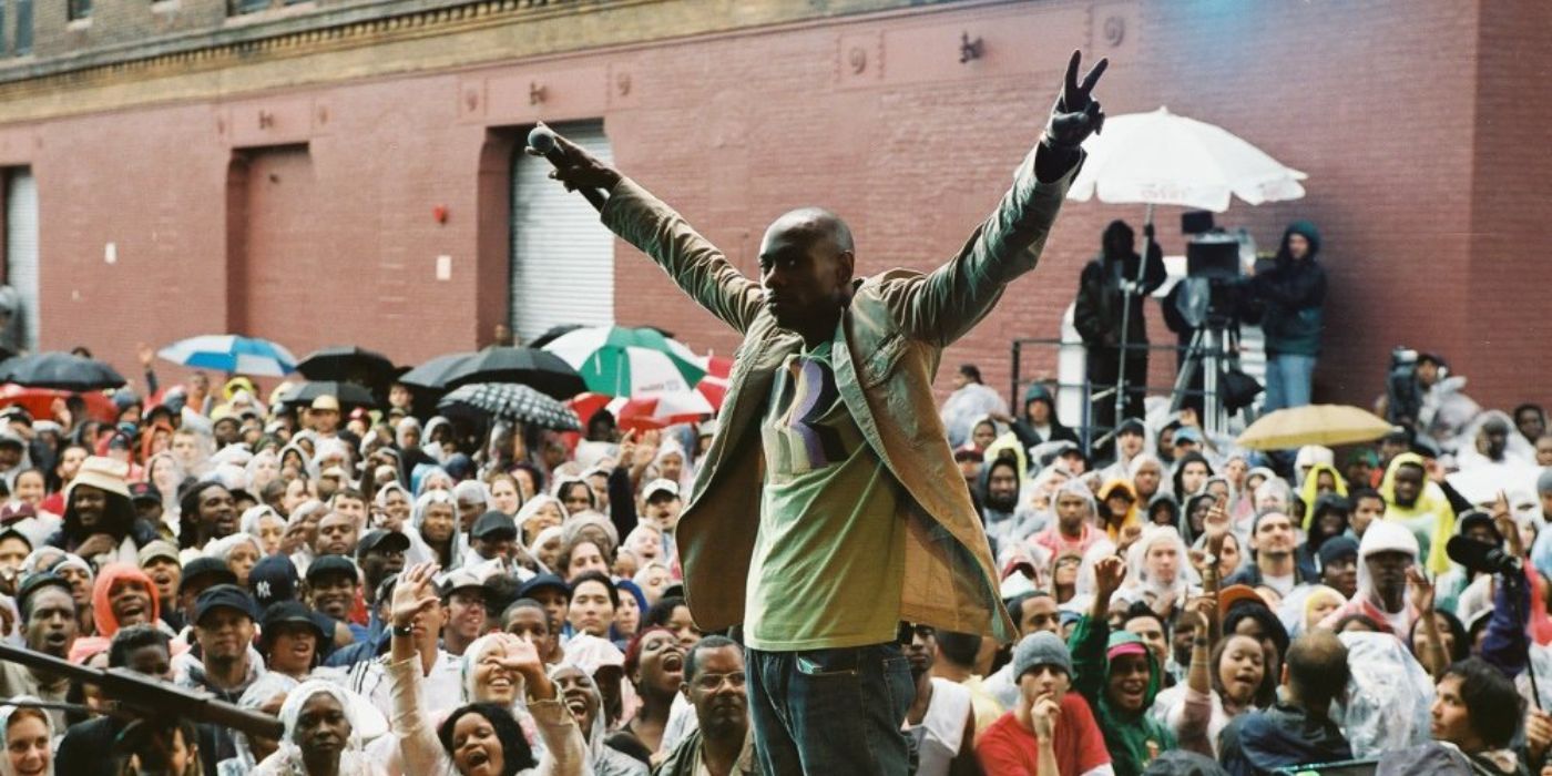 Dave Chappelle stands on an open-air stage with a large crowd in attendance in Dave Chappelle's Block Party.