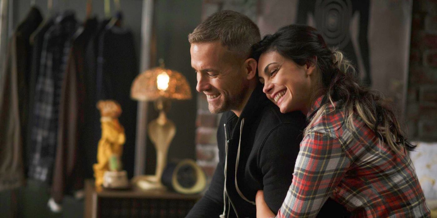 Wade Wilson (Ryan Reynolds) and Vanessa (Morena Baccarin) smiling as Vanessa holds onto his right arm and leans into him, in Deadpool 1