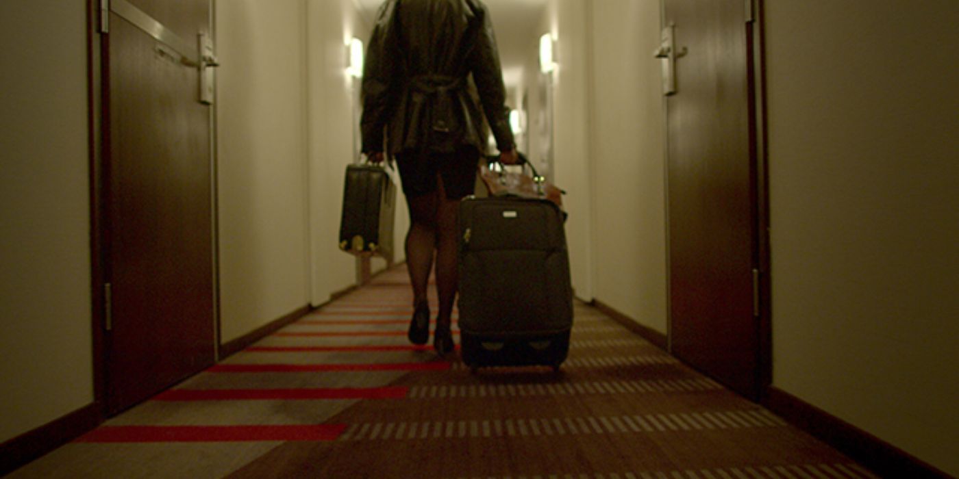 A woman walks down a hotel hallway with luggage trailing behind her