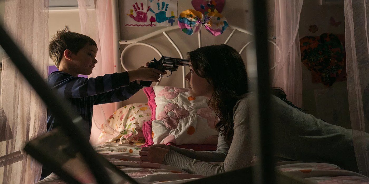 Emelie, played by actor Sarah Bolger, leans across a bed while Christopher, played by actor Thomas Bair, points a gun at her in Emelie.