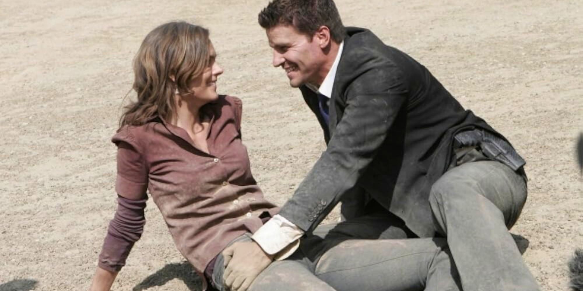 Emily Deschanel sitting on the ground covered in dirt looking at David Boreanaz sitting next to her next to her in Bones episode Aliens in a Spaceship.