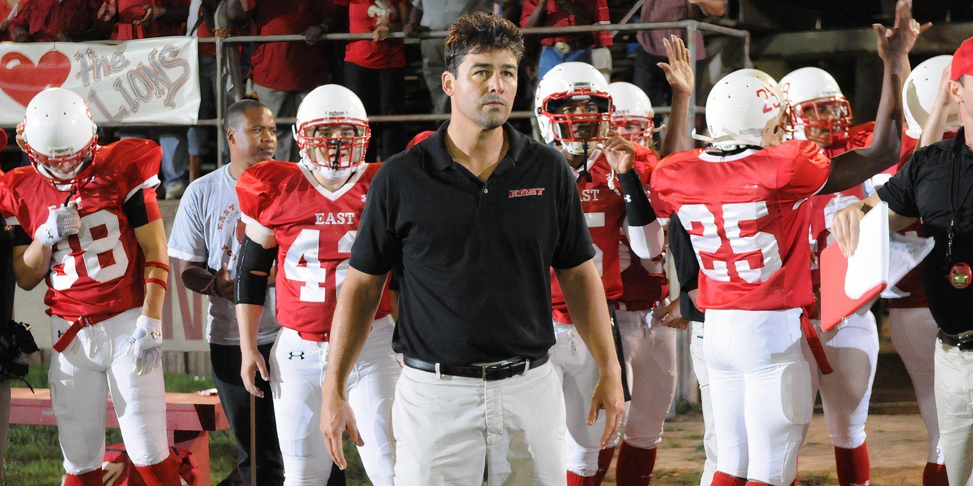 Kyle Chandler as Coach Taylor standing in front of his players on the sideline at a football game on Friday Night Lights.