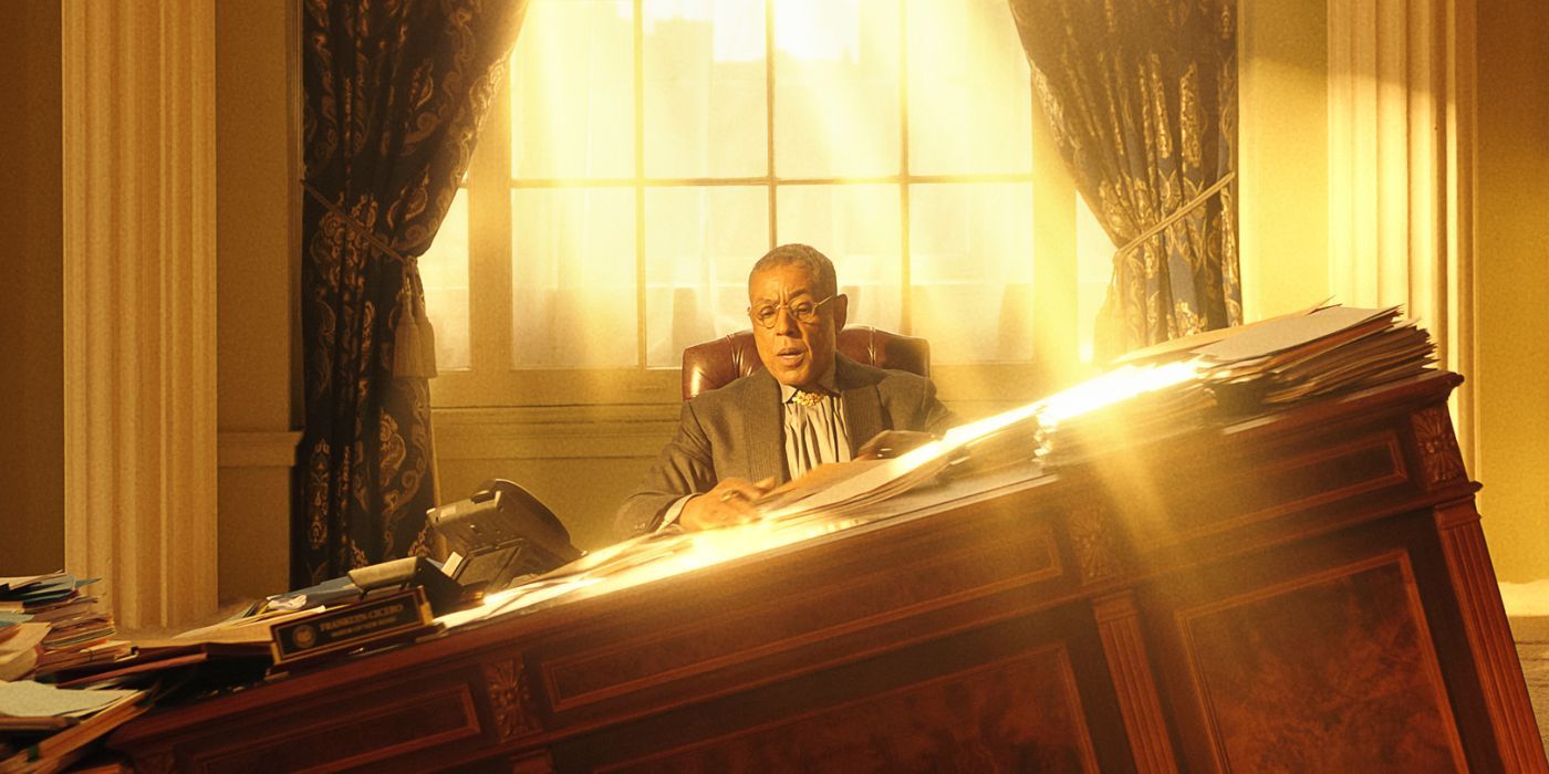 Giancarlo Esposito sitting behind a sinking brown wooden desk in Megalopolis.