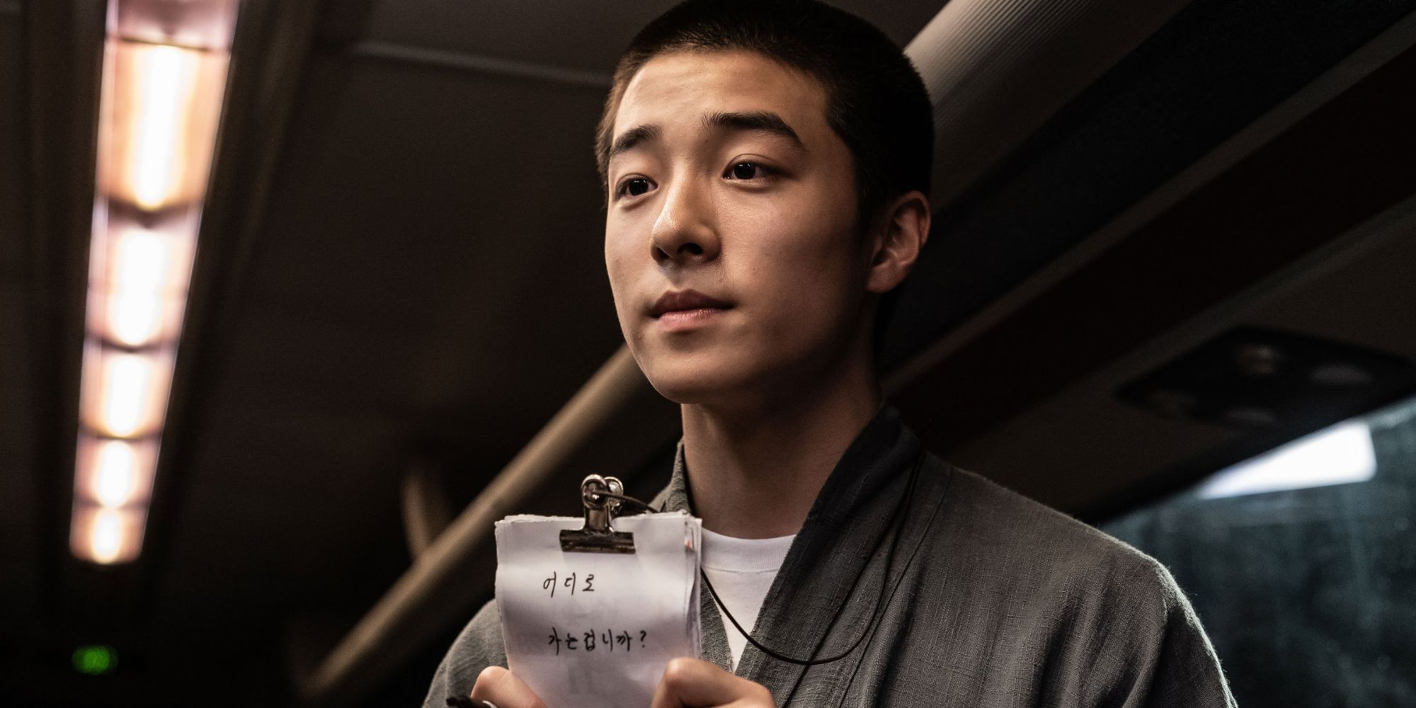 A young man looks earnest and holds a note written in Korean in The 8th Night.