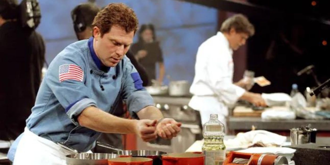 Bobby Flay cooks at a station with a competitor cooking in the background on Iron Chef America.