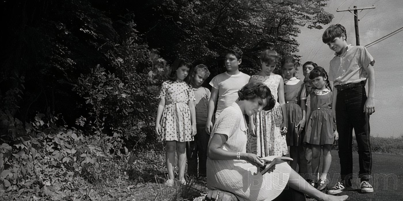 A group of children around a woman witting on the ground reading in Ladybug Ladybug 2