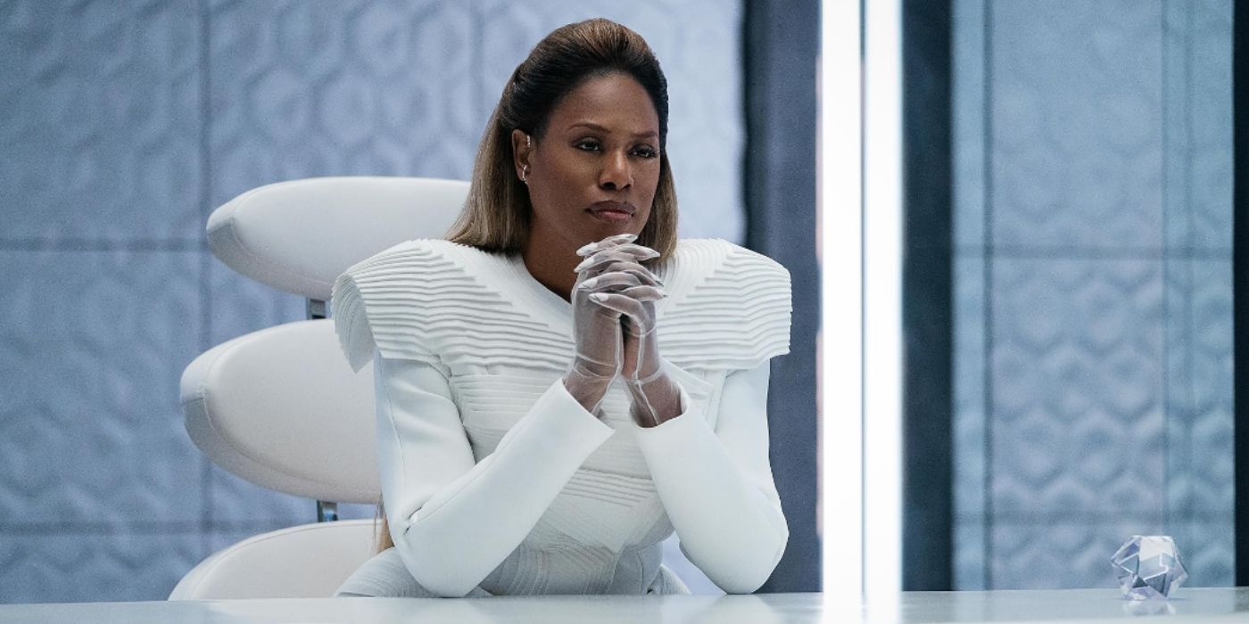 En Uglies, Laverne Cox viste un traje futurista blanco y se sienta en un escritorio blanco.