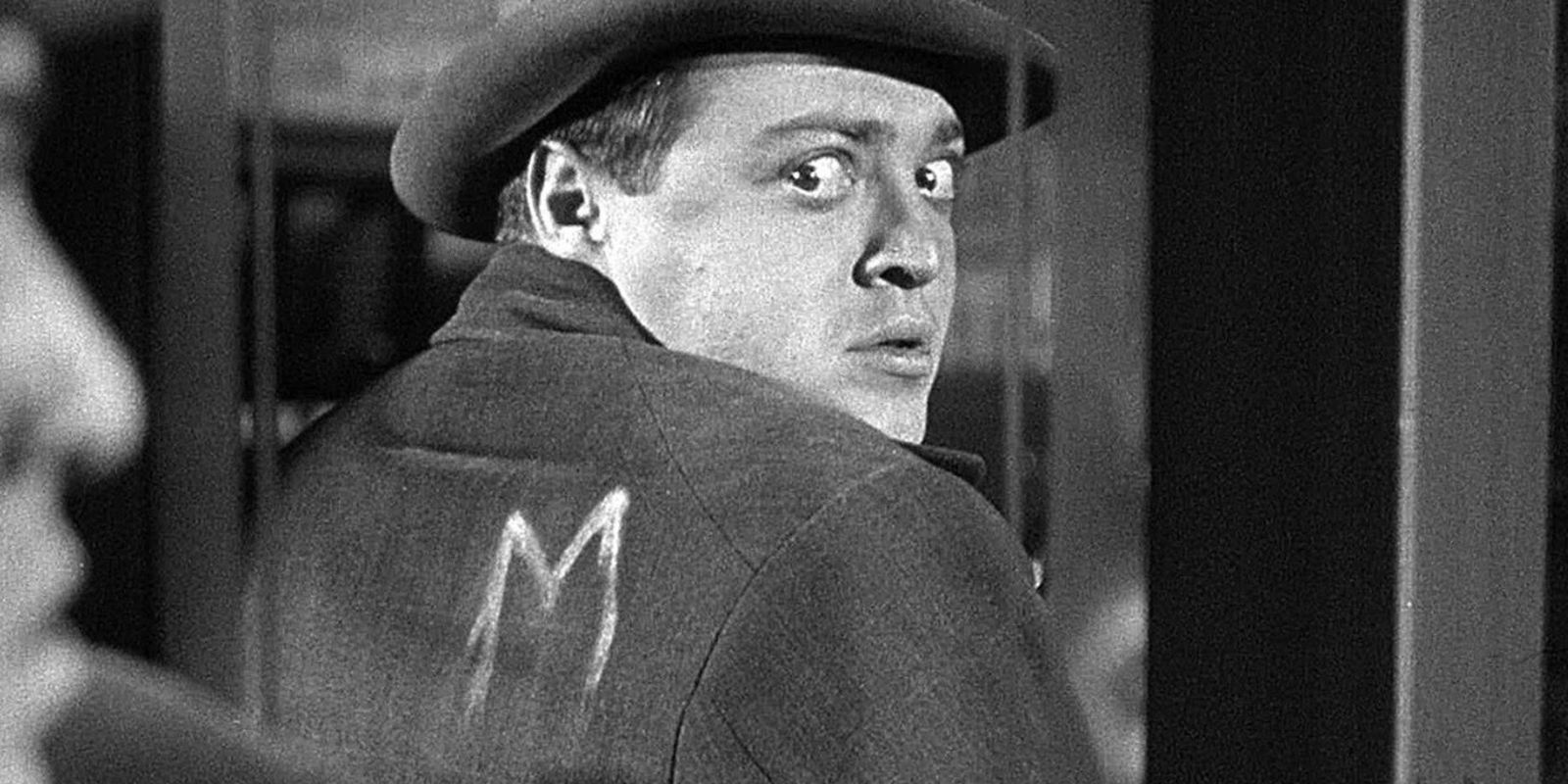 A man uses a mirror to look at his own back, where he sees a chalk letter &lsquo;M&rsquo; written on his coat
