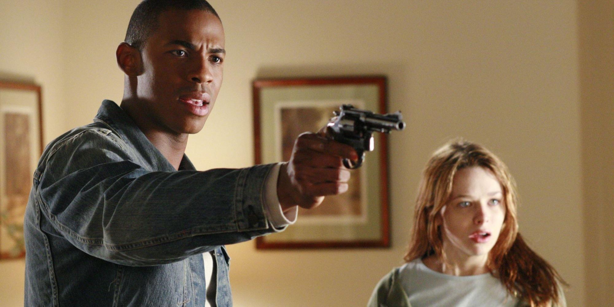 Mehcad Brooks holding a gun out in front of him while Joy Jorgensen stands behind him