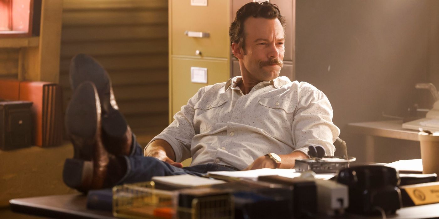 Kyle Schmid with his feet up on a desk in an office in a scene from NCIS: Origins.