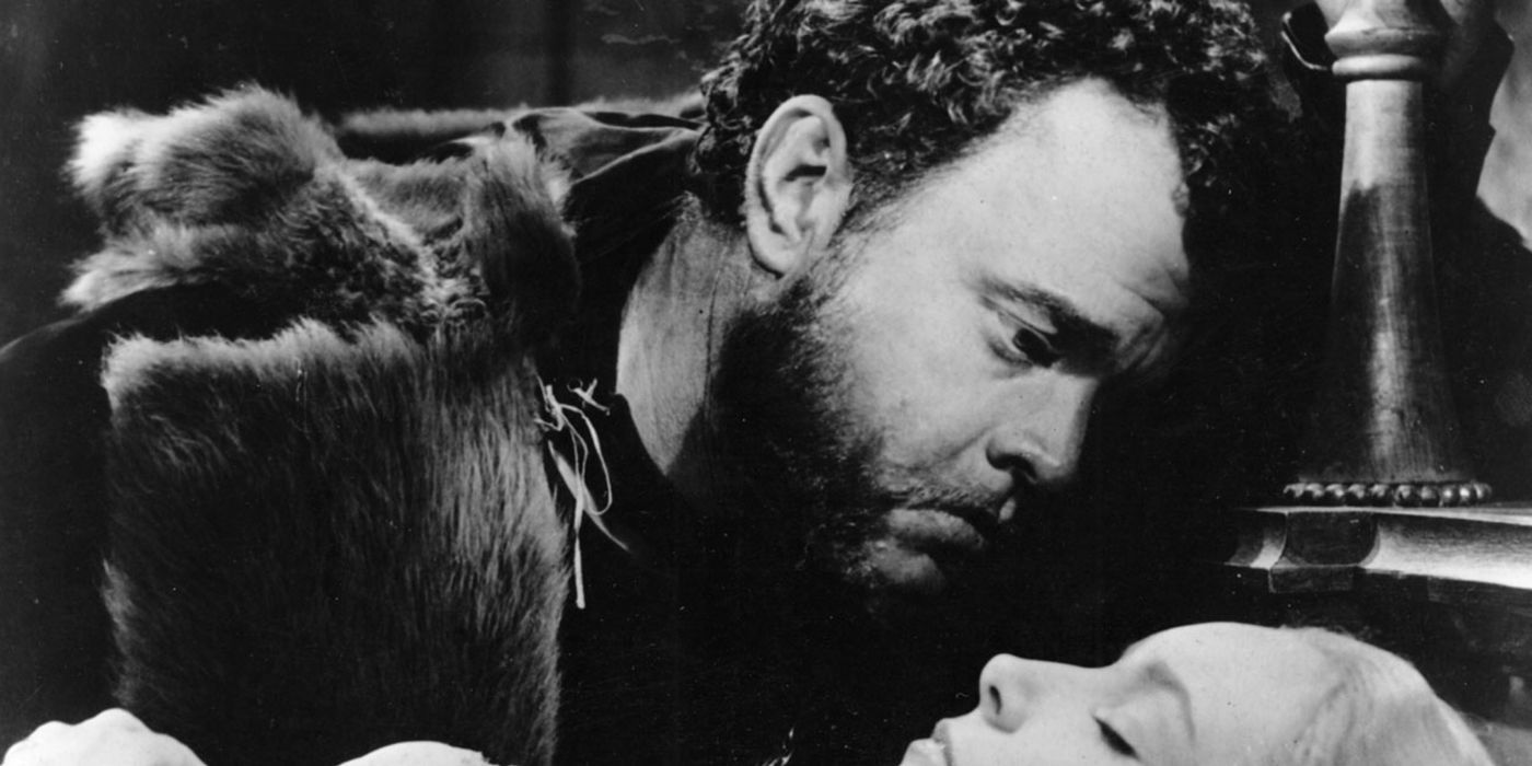 Orson Welles as Othello in Othello looking down while leaning over a sleeping woman with a concerned expression