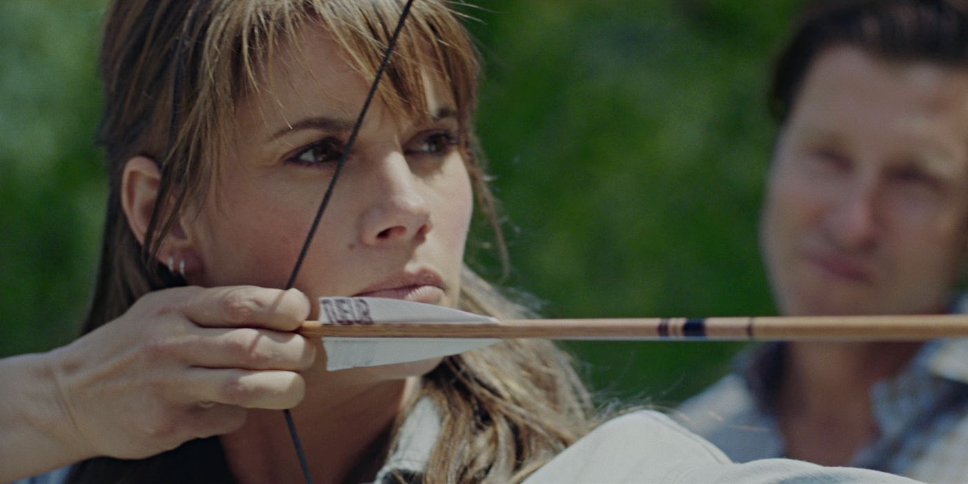 Missy Peregrym as Sophie, aiming a bow and arrow while Damon Runyan as Nolan watches in the background in Out Come the Wolves