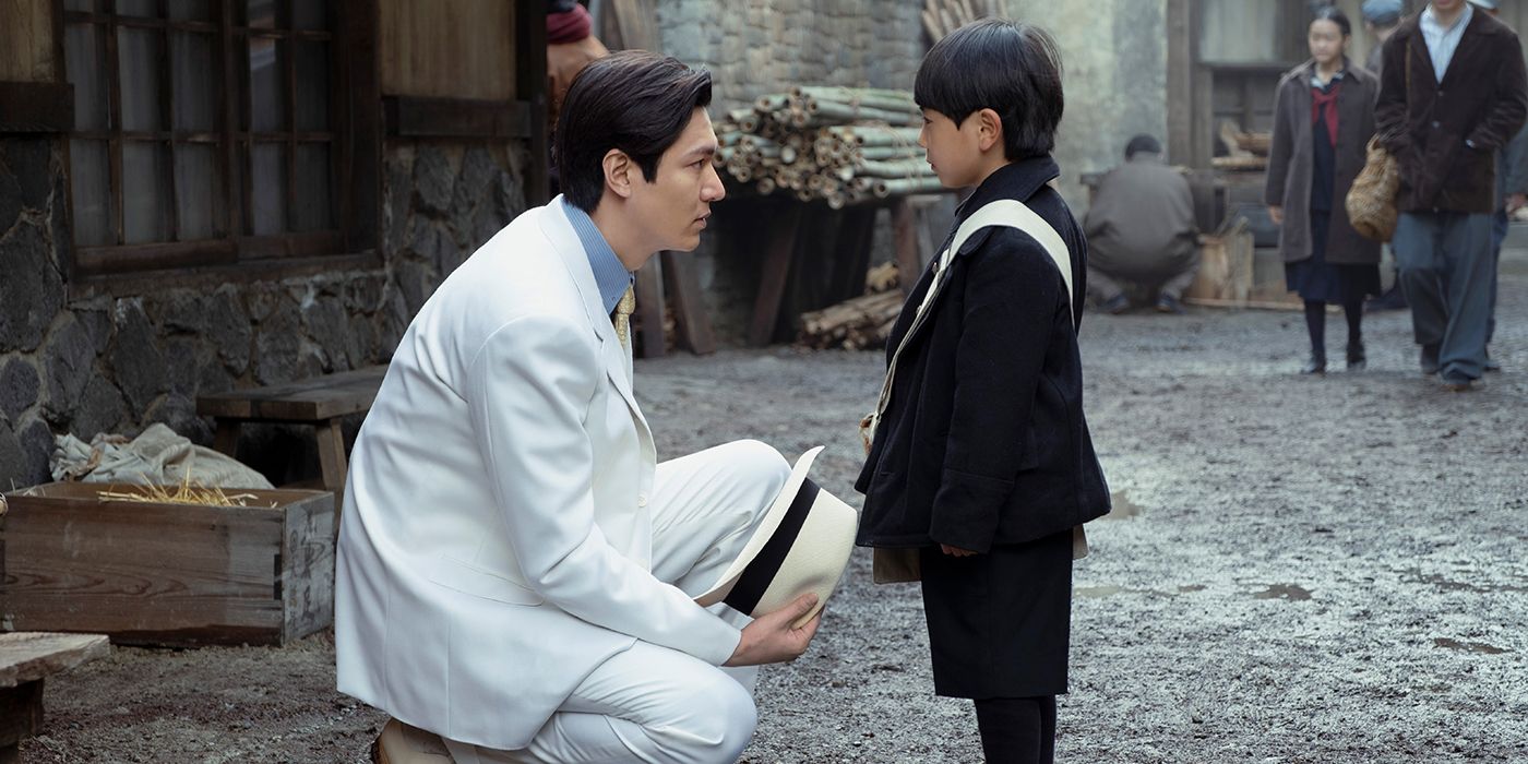 Lee Minho as Hansu in a white suit crouching down to talk to Jae Jun Park as young Noa in the street in Pachinko Season 1