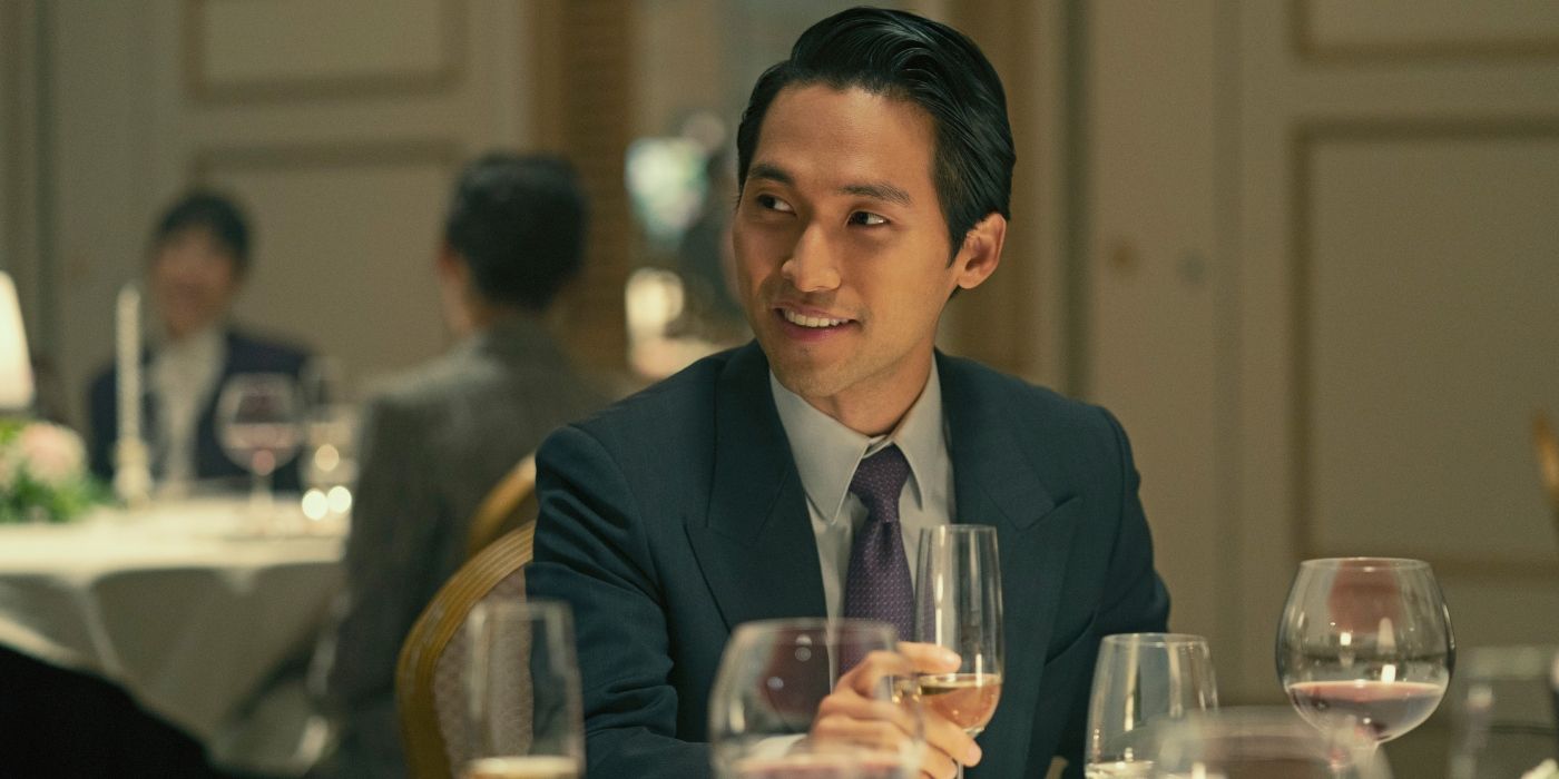 En una escena de Pachinko, Solomon (Jin Ha) está sentado a la mesa con una copa de vino frente a él.