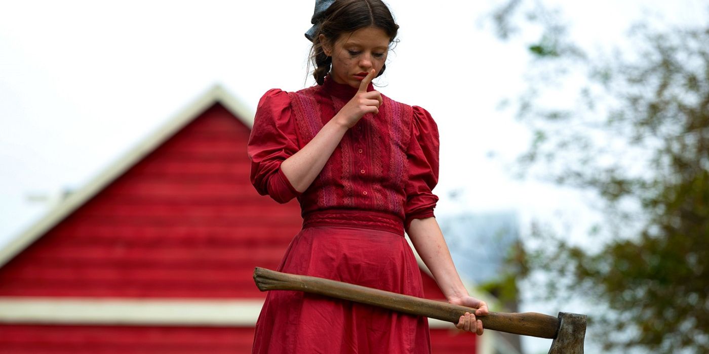 Mia Goth as Pearl holding an axe and hushing someone while wearing a red dress. 