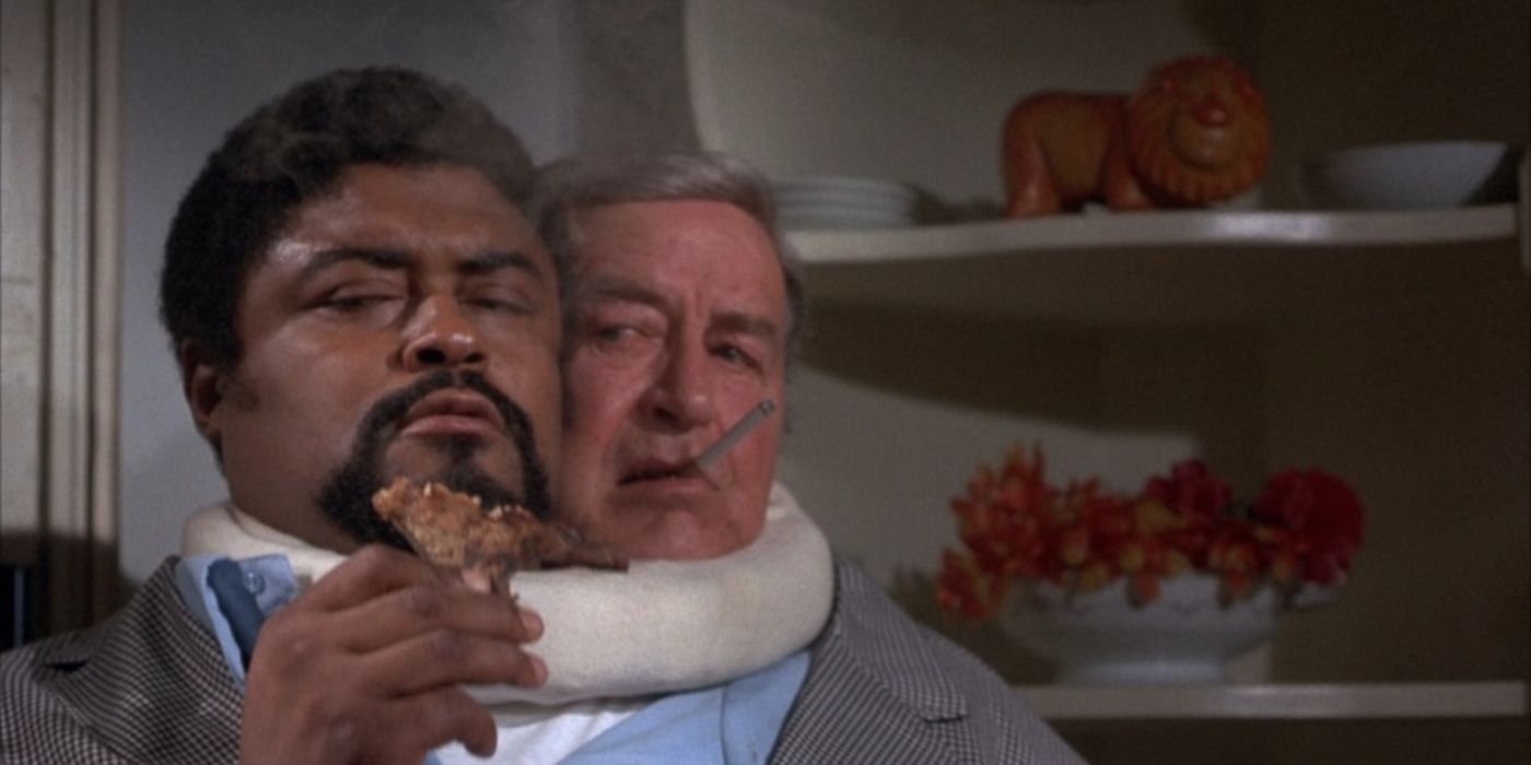 On a body with two heads, one smokes a cigarette while the other tries to eat a piece of food in The Thing with Two Heads (1972)