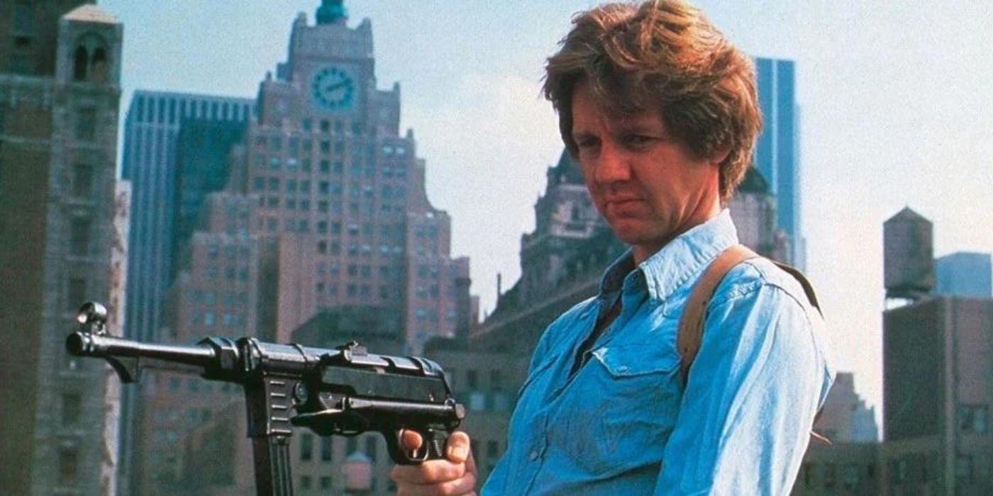 A man in a button down with the city skyline behind him points an automatic weapon at someone off-camera